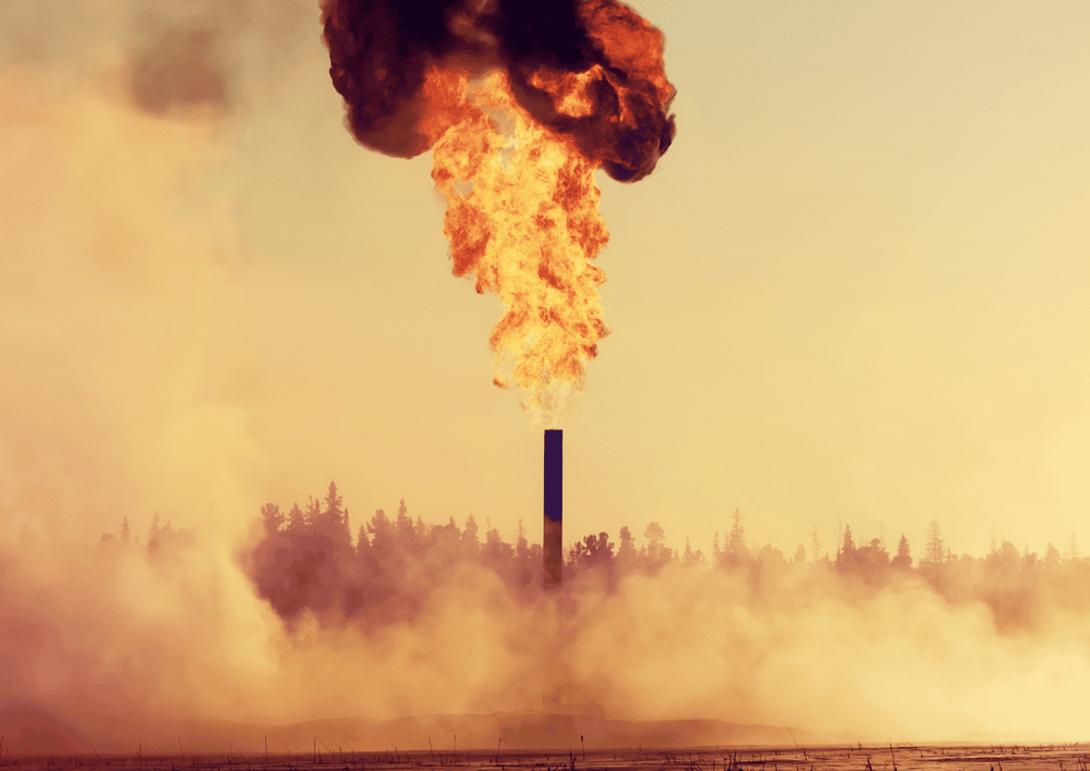 Image of a oil well spitting fire, with pollution in the foreground and a forest in the background.