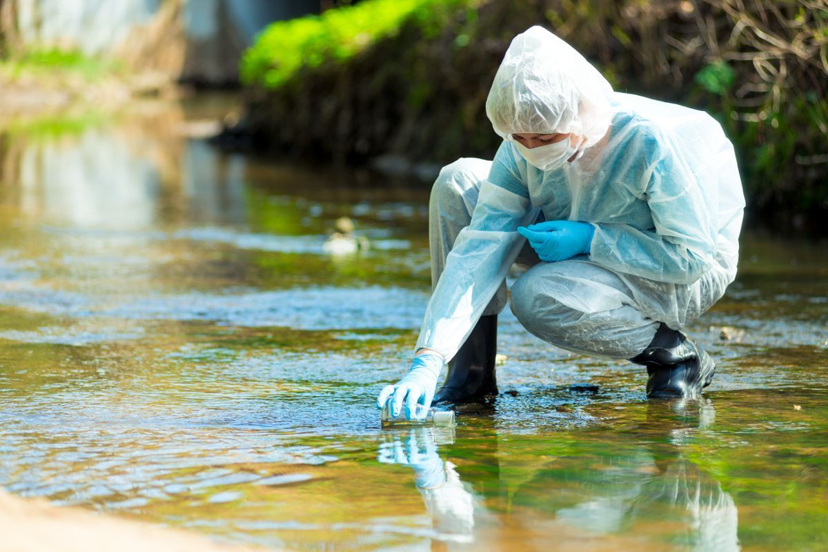 scientists takes a water sample from a small river to detect if it is contaminated by forever chemicals 