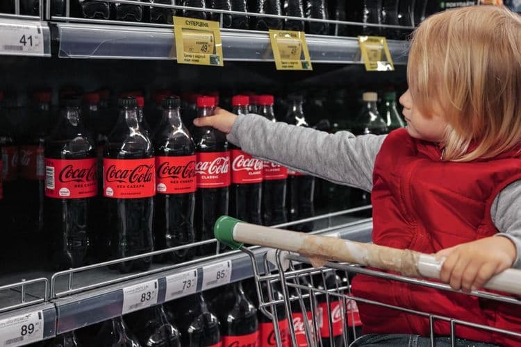a child taking a Coca-Cola from a supermarket shelf