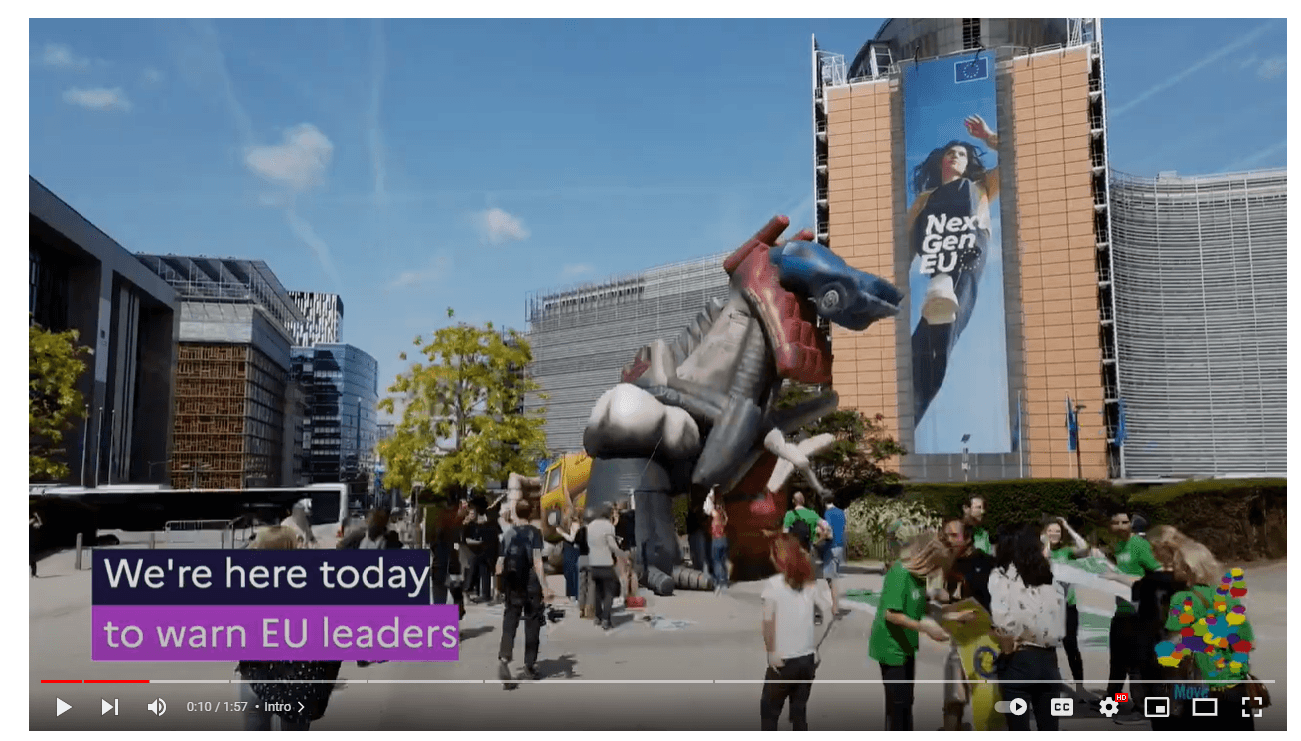 Captura de pantalla del vídeo realizado por Movemos Europa, en el que se ve un inmenso dinosaurio hinchable, creado con objetos que representan los combustibles fósiles (bidones de crudo, un coche un avión, nubes de humo...) ante la Comisión Europea y un grupo de activistas con pancartas